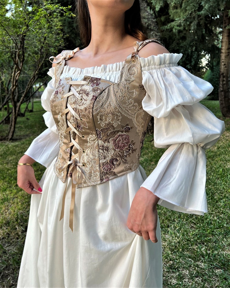 May include: A white off-the-shoulder peasant top with puffed sleeves and a brown and gold brocade corset with a lace-up front.