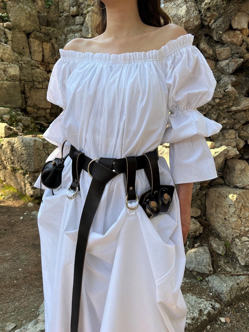 May include: A white off-the-shoulder peasant top with long sleeves and a black leather belt with decorative metal rings and pouches.