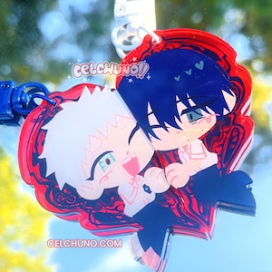 Pode incluir: Um chaveiro de acrílico de dupla face com dois personagens em estilo anime se abraçando. Um personagem tem cabelo branco, o outro tem cabelo azul. O chaveiro tem uma borda vermelha com o texto "CELCHUNO!!" e "CELCHUNO.COM".