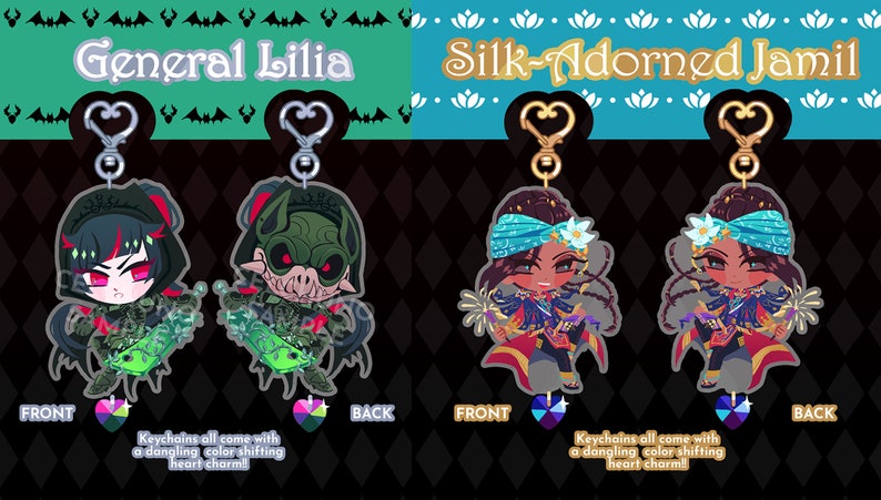 May include: Two double-sided acrylic keychains featuring anime characters. The first keychain features General Lilia, a green-skinned character with bat wings and a sword. The second keychain features Silk-Adorned Jamil, a brown-skinned character with blue and gold clothing and a flower in their hair. Both keychains come with a dangling color-shifting heart charm.
