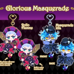 May include: Two character keychains featuring the characters Rollo Flamme and Masquerade Idia from the anime Twisted Wonderland. The keychains are in a chibi style and feature the characters in their masquerade outfits. The keychains come with a dangling heart charm.