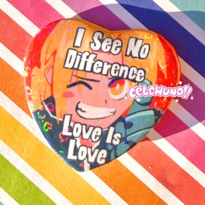 May include: A heart-shaped button with a cartoon character with blonde hair and orange eyes. The button has a rainbow glitter background and the text "I See No Difference Love Is Love" and "celchuno!!".