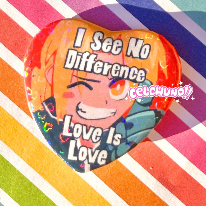 May include: A heart-shaped button with a cartoon character with blonde hair and orange eyes. The button has a rainbow glitter background and the text "I See No Difference Love Is Love" and "celchuno!!".