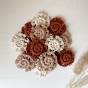 May include: A collection of handmade macrame wall hangings in various shades of brown, beige, and white. The hangings are circular and feature a knotted design.