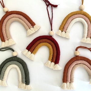 May include: A set of seven colorful macrame rainbow wall hangings with wooden beads and white tassels. The rainbows are made with different colored cords, including red, orange, yellow, green, blue, and purple.