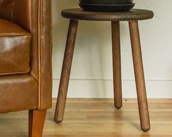May include: A brown leather armchair with a tufted back and a wooden base sits next to a small wooden stool with a potted snake plant on top. The plant has long, green leaves with yellow stripes.