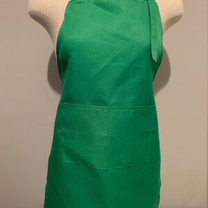 Pu&ograve; includere: Un grembiule verde tinta unita con una tasca sul davanti. Il grembiule ha spalline regolabili con una fibbia.