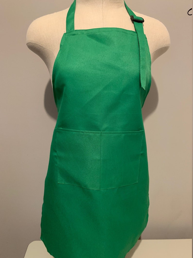 Pu&ograve; includere: Un grembiule verde tinta unita con una tasca sul davanti. Il grembiule ha spalline regolabili con una fibbia.