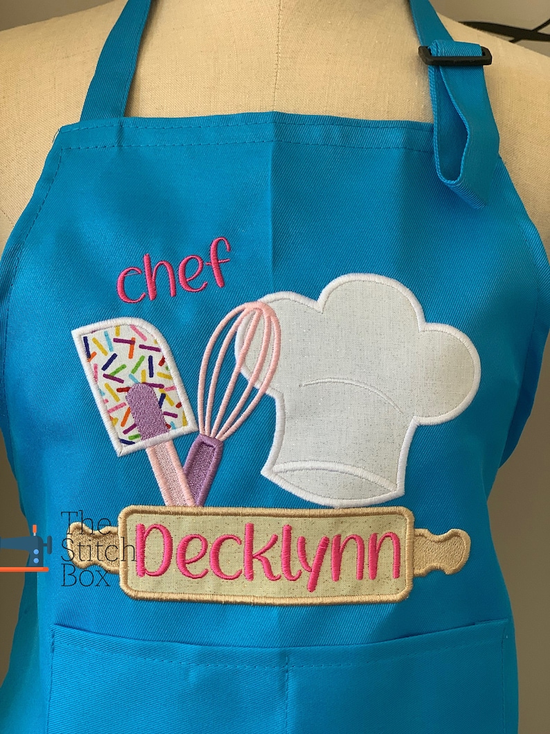 Pu&ograve; includere: Un grembiule da chef blu turchese con un cappello da chef bianco, una frusta rosa e bianca, una spatola rosa e bianca con codette e un mattarello con il nome "Decklynn" ricamato. Il grembiule ha anche la parola "chef" ricamata.