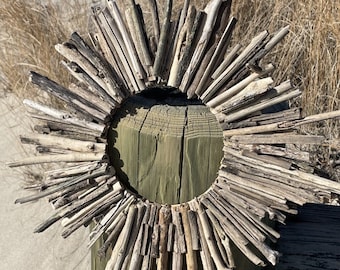 May include: A rustic wreath made of driftwood branches, arranged in a circular shape, mounted on a wooden post. The wreath is a natural, beach-inspired decoration.