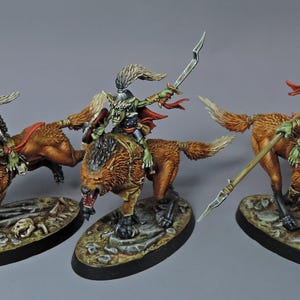 Puede incluir: Tres figuras en miniatura de jinetes goblin sobre lobos. Los goblins tienen piel verde y llevan cascos y armaduras. Los lobos son marrones con pelaje detallado. Cada figura está montada sobre una base ovalada.