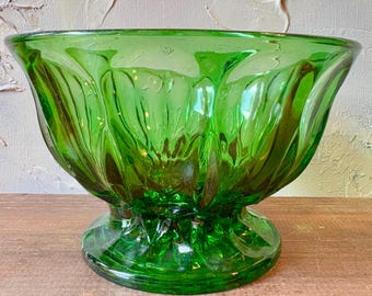 May include: A vibrant green glass bowl with a pedestal base. The bowl has a wide, fluted design and a glossy finish. The bowl is a decorative piece, perfect for serving or display.
