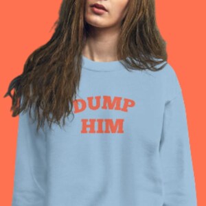 K&ouml;nnte beinhalten: Ein hellblauer Pullover mit dem Text "DUMP HIM" in Orange.