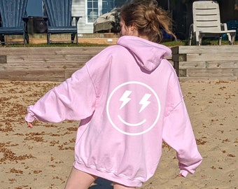 Könnte beinhalten: Ein rosa Hoodie mit einem weißen Smiley mit Blitzen auf der Rückseite.