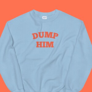 K&ouml;nnte beinhalten: Hellblauer Pullover mit dem Text "DUMP HIM" in Orange.