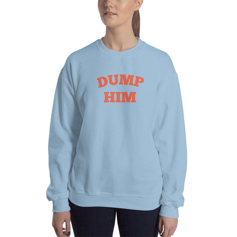 K&ouml;nnte beinhalten: Ein hellblauer Pullover mit dem Text "DUMP HIM" in Orange.