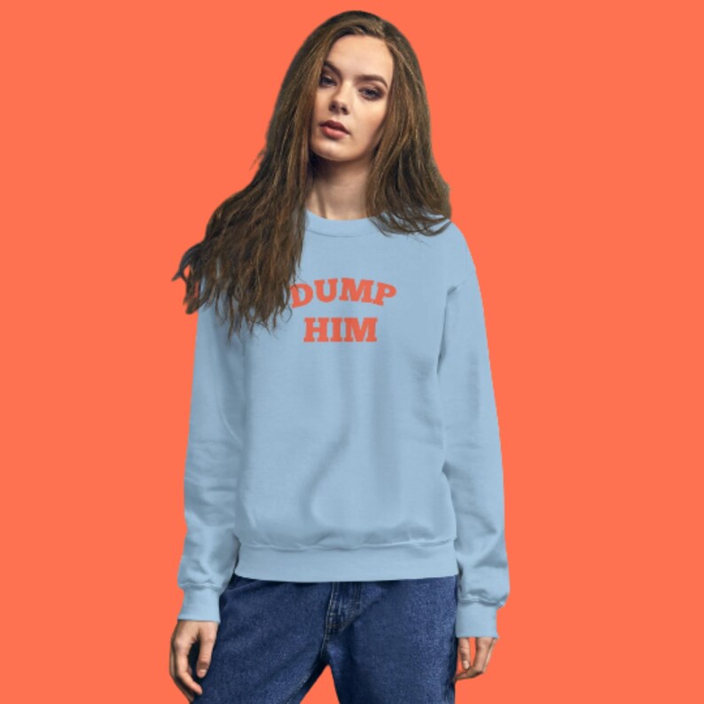 K&ouml;nnte beinhalten: Ein hellblauer Pullover mit dem Text "DUMP HIM" in Orange.