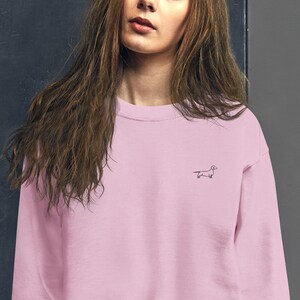 May include: A pink crew neck sweatshirt with a small black dachshund outline embroidered on the front.