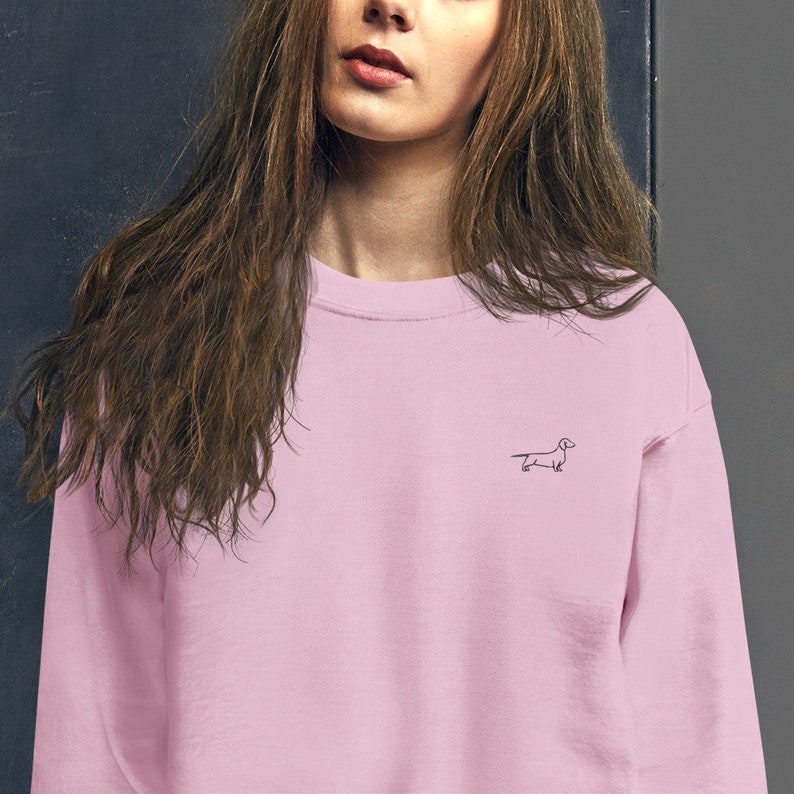 May include: A pink crew neck sweatshirt with a small black dachshund outline embroidered on the front.