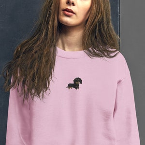 Op de afbeelding: Een roze sweatshirt met een klein geborduurd beeld van een zwarte teckel.