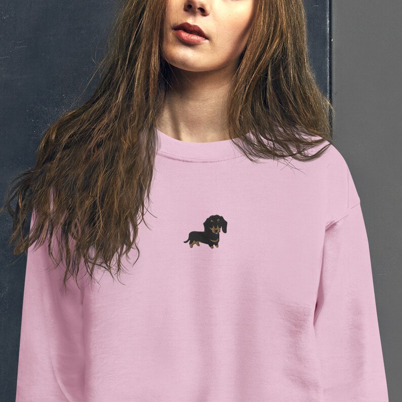 Op de afbeelding: Een roze sweatshirt met een klein geborduurd beeld van een zwarte teckel.