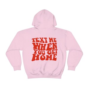 K&ouml;nnte beinhalten: Rosa Kapuzenpullover mit dem Text "TEXT ME WHEN YOU GET HOME" in roten, Retro-Lettern.