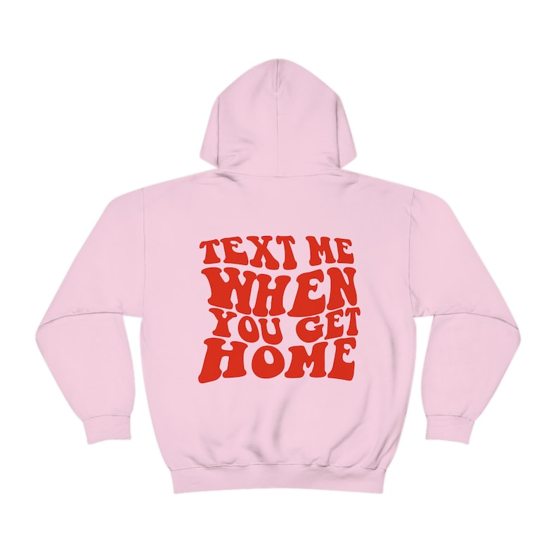 K&ouml;nnte beinhalten: Rosa Kapuzenpullover mit dem Text "TEXT ME WHEN YOU GET HOME" in roten, Retro-Lettern.