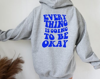 Könnte beinhalten: Grauer Kapuzenpullover mit dem Text "EVERY THING IS GOING TO BE OKAY" in blauen Buchstaben auf der Rückseite.
