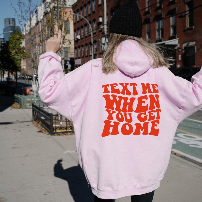 K&ouml;nnte beinhalten: Rosafarbener Hoodie mit einem roten Aufdruck, der in einer Retro-Schrift "Text Me When You Get Home" sagt.