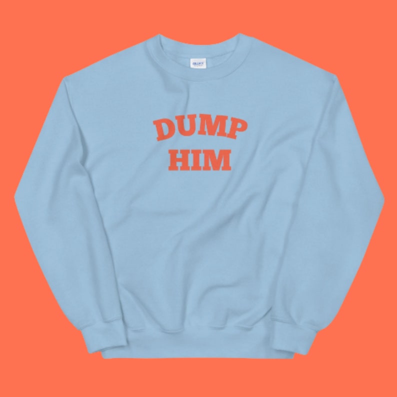 K&ouml;nnte beinhalten: Hellblauer Pullover mit dem Text "DUMP HIM" in Orange.