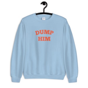 K&ouml;nnte beinhalten: Hellblauer Pullover mit dem Text "DUMP HIM" in Orange.