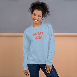 K&ouml;nnte beinhalten: Ein hellblauer Pullover mit dem Text "DUMP HIM" in Rot.