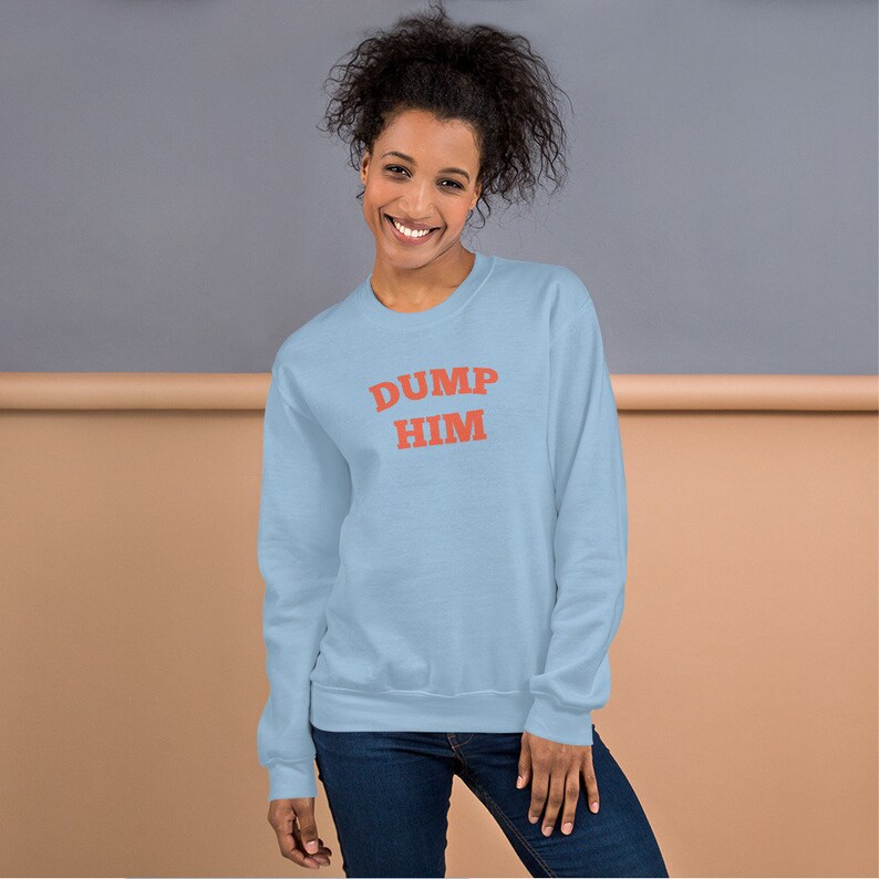 K&ouml;nnte beinhalten: Ein hellblauer Pullover mit dem Text "DUMP HIM" in Rot.