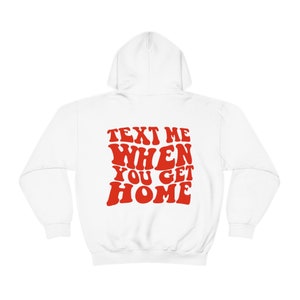 K&ouml;nnte beinhalten: Wei&szlig;er Kapuzenpullover mit dem Text "TEXT ME WHEN YOU GET HOME" in roten, retro-artigen Buchstaben.