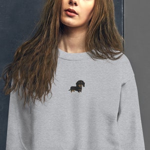 Op de afbeelding: Een grijs sweatshirt met een geborduurde zwarte en bruine teckel op de voorkant.