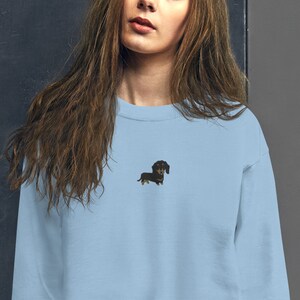 Op de afbeelding: Een lichtblauw sweatshirt met een zwarte teckel geborduurd op de voorkant.