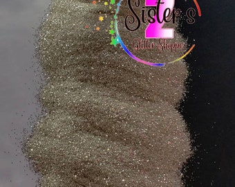 May include: A close-up of a pile of silver glitter. The glitter is loose and has a slight iridescent sheen. The glitter is labeled "Sister's Glitter Shoppe".