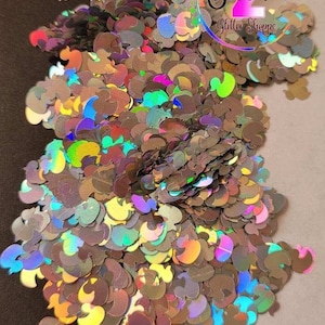 May include: A large pile of iridescent holographic duck shaped glitter. The glitter is a mix of gold, silver, and rainbow colors.