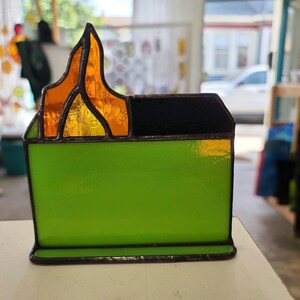 Peut inclure: Une sculpture en verre coloré représentant une poubelle verte avec une flamme sur le dessus. La flamme est faite de verre orange et jaune.