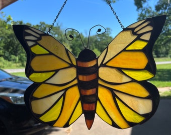 May include: A stained glass butterfly window hanging with a chain. The butterfly is yellow with black and brown accents.