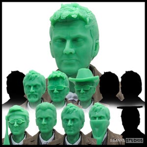 May include: A collection of green resin 3D printed head sculpts featuring various facial expressions, hairstyles, and accessories like hats, glasses, and face coverings. The text EBANK STUDIOS is visible in the bottom right corner of the image.