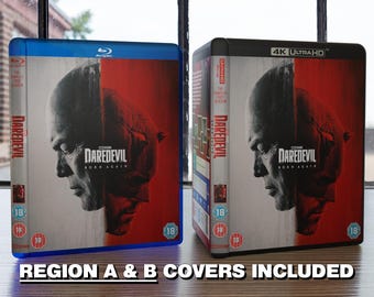 May include: Two Blu-ray disc cases for the movie Daredevil: Born Again. The left case is a standard Blu-ray case with a blue spine and the right case is a 4K Ultra HD Blu-ray case with a black spine. Both cases feature the same image of Daredevil's face with a red and white background. The text "Daredevil: Born Again" is printed on both cases.