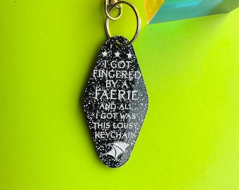 May include: Black keychain with silver glitter and the text "I got fingered by a faerie and all I got was this lousy keychain".