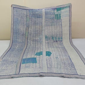 May include: A vintage, handmade quilt with a blue and white color scheme. The quilt features a patchwork design with visible stitching and a textured appearance. The edges are finished with a contrasting border, adding to its rustic charm.
