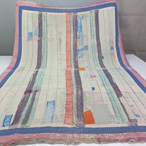 May include: A rectangular textile featuring a cream-colored base with vertical stripes in shades of blue, purple, and red. The fabric displays visible stitching patterns and scattered rectangular patches in orange, blue, and gray, finished with a pink border.