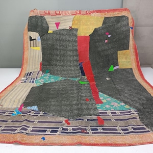 May include: A rectangular textile featuring a patchwork design of various fabric scraps in shades of charcoal gray, yellow, red, and teal. The piece includes striped patterns, floral prints, and solid blocks, all bordered by a wide, orange-red trim.