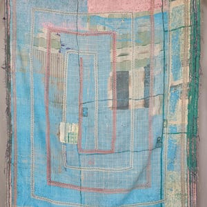 May include: A rectangular textile blanket featuring a patchwork of light blue, pink, and green fabric panels. The surface is covered in dense, visible running stitch embroidery in white and pink thread, forming a large spiral pattern across the center.