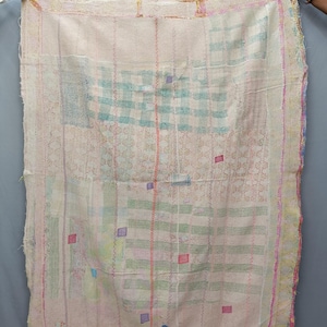 May include: A cream-colored, hand-stitched quilt with a patchwork design. The quilt features a mix of colors, including pink, green, and blue, with a variety of patterns and textures. The edges are finished with a pink border.