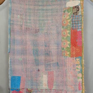 Puede incluir: Una manta rectangular con un diseño de patchwork que combina diversos patrones de tela en tonos azul claro, rosa y blanco. La superficie está cubierta por densas costuras visibles en toda la pieza, lo que le otorga una apariencia texturizada.