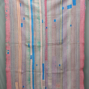 May include: A rectangular textile throw featuring a patchwork of vertical stripes in shades of pink, lavender, grey, and blue. The fabric displays visible running stitch patterns throughout, with small rectangular blue patches and a tag reading Art DD 10226.